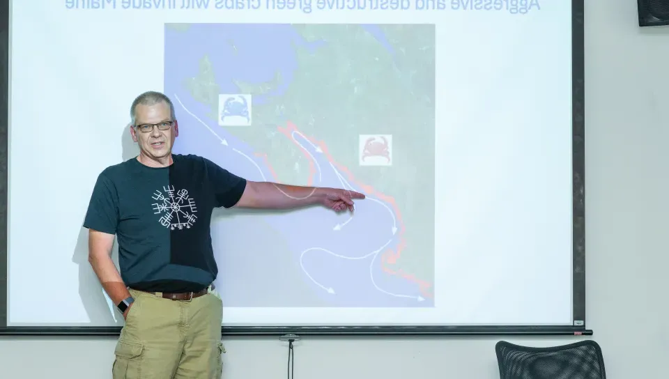 UNE's Markus Frederich points to a map on a slideshow presentation